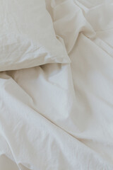 Beige cotton bedding sheet, and pillow. Minimal bed concept. Flat lay, top view.