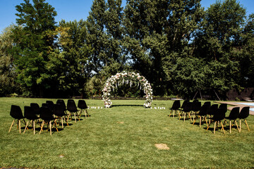 Wedding ceremony aisle with an arch made of chiffon white textile and flowers and long white wooden...