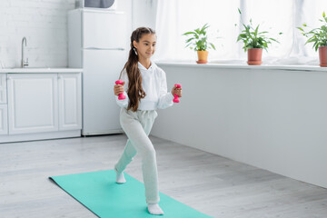 Preteen kid with dumbbells training on fitness mat at home