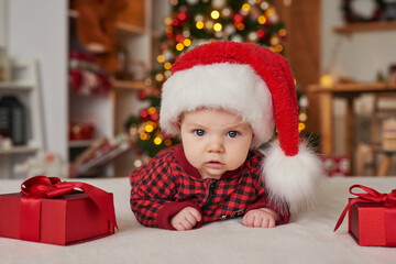 Fototapeta na wymiar Christmas baby boy in santa hat on background of christmas tree with gifts.