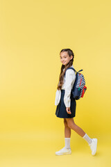 Fototapeta na wymiar Preteen pupil with backpack smiling at camera on yellow background