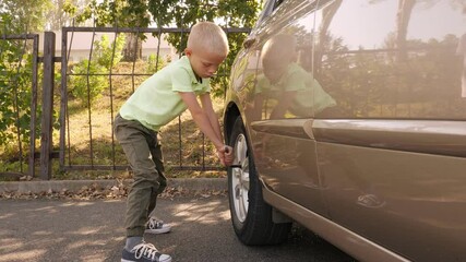 A little boy of eight years old is fixing a wheel on a car, he is trying to unscrew the bolts on the wheel to replace the tires.