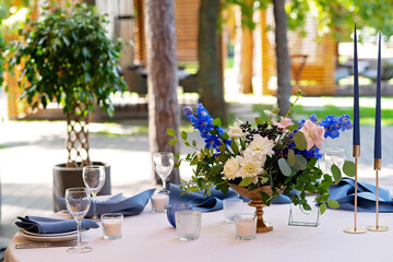 Fototapeta na wymiar Festive wedding, table setting with blue linen napkins, candles and fresh flower bouquets. Wedding decorations. Restaurant menu concept. Soft selective focus.