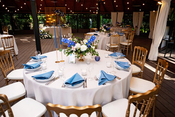 Festive wedding, table setting with blue linen napkins, candles, golden chairs, and fresh bouquets of flowers. Wedding decorations. Restaurant menu concept. Soft selective focus.