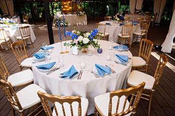 Festive wedding, table setting with blue linen napkins, candles, golden chairs, and fresh bouquets of flowers. Wedding decorations. Restaurant menu concept. Soft selective focus.