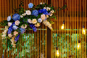 Wedding presidium, banquet table for newlyweds with flowers, greenery, blue and gold color. Lush flower arrangement on the wedding table. Glowing light bulbs. Soft selective focus.
