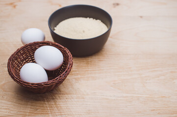 dark gray stoneware bowl with whole wheat flour and white eggs on a rustic wooden tabletop
