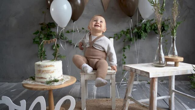 first happy birthday kid on festive background of balloons and cake, birthday one year in rustic style, little boy sitting on a name day chair, toddler photo. Children birthday concept.