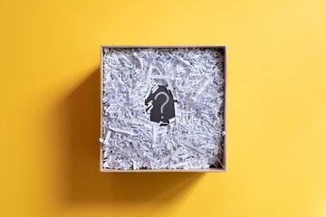 Question mark and shredded paper in abox against yellow background. Concept of Questions, recycle and secret