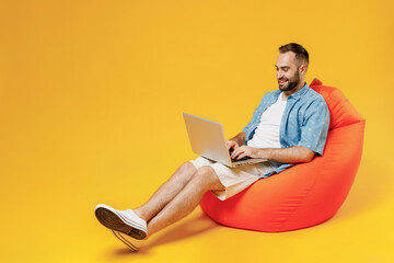 Full body young smiling happy man 20s wear blue shirt white t-shirt sit in bag chair hold use work...