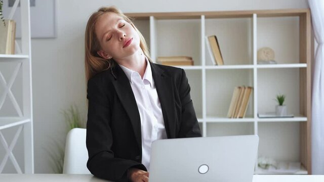 Tired woman. Distance work. Office workout. Exhausted elegant lady stretching neck after typing on laptop sitting light room interior.