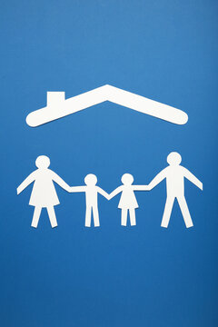 Happy paper family with roof on blue background with copy space. Family day. Vertical photo.