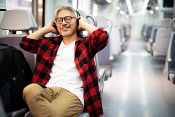 Senior man traveling by train. Man listening the music while enjoying in travel.