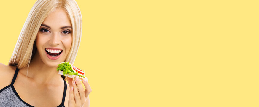 Woman In Sportswear Holding сrispbread Sandwich With Cheese, Tomato And Salad, Isolated Over Yellow Color Background. Slim Blond Girl At Studio Shot. Health, Beauty And Dieting Concept.