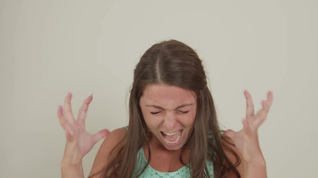 Chubby young adult woman screaming, raising hands up, starting to hyperventilate, expressing anger, fury against white background indoors. Stressed lady showing negative emotions