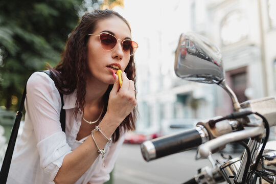 Fototapeta Young woman paints her lips looking in the mirror of a motorcycle.
