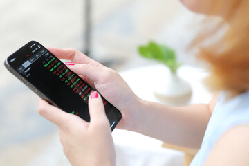 Female hand with smartphone trading stocks online in coffee shop Business concept