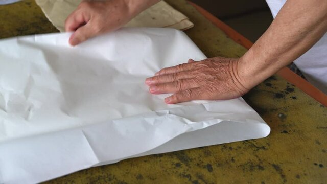 An old calligrapher prepares to fold the rice paper before writing the calligraphy