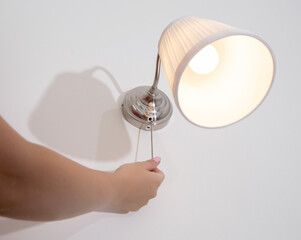 A woman's hand turns the wall sconce on and off with a rope. Night light above the bed, close-up