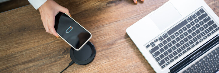 Charging mobile phone battery with wireless charging device in the table. Smartphone charging on a...