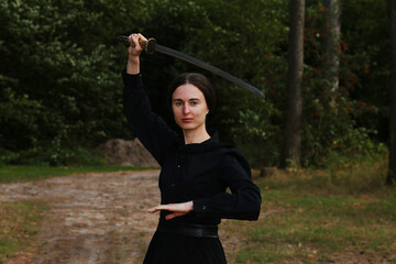 Woman in black classic clothes with katana sword in the forest