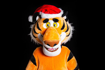 Plush soft orange tiger in a red santa claus hat on a black background. Christmas and new year 2022 concept