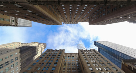 Wide angle panorama of blue sky with clouds between two rows of New York City Midtown buildings
