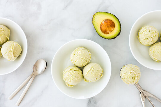 Avocado Ice Cream in Bowls, Ice Cream Scoop and Avocado on White Marble