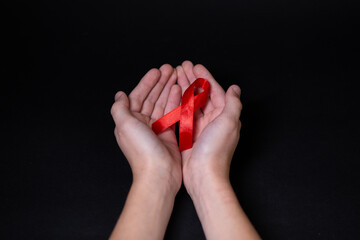 Child human hands hold red ribbon symbol of AIDS on a black background