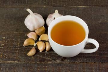 Garlic tea in ceramic cup with garlic on rustic wooden background.