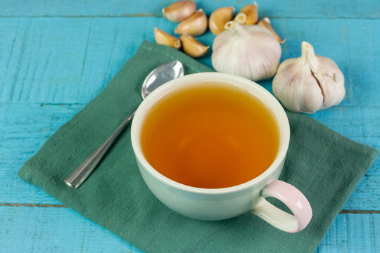 Garlic tea in ceramic cup with garlic on blue wooden background.