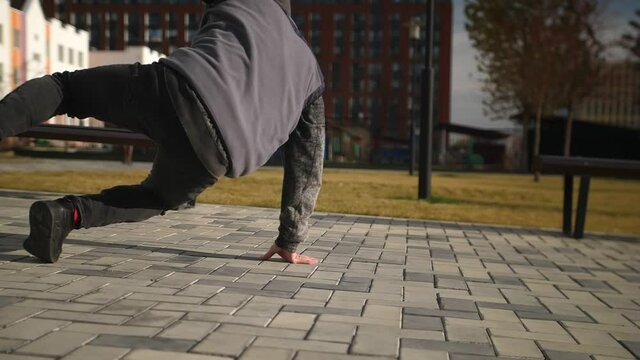 A man in gray clothes dancing breakdancing. A man in a hood dances in the middle of the city quarter