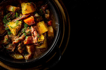 Goulash. Vegetable rague with meat, eggplant, pepper, potato and carrot in black bowl on dark wooden background