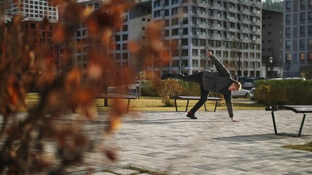 Dancer stands on one hand in slow motion in a picturesque city block. Hand freeze