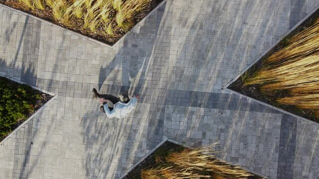 A man is actively dancing breakdancing against the background of wheat and street gray tiles. Breakdancer in a denim jacket and black pants is engaged in active dance in the fall.