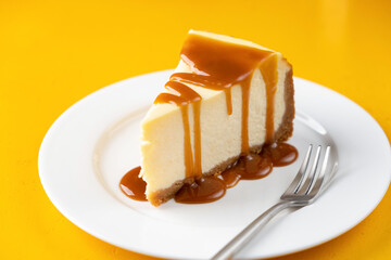 Slice of cheesecake with salted caramel sauce on plate, isolated on yellow background