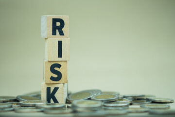 Stack of vertical wooden blocks with the word with a letter Risk and many coin on ground. The...