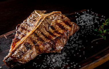 Grilled T-bone Steak on bones on wooden board on dark background