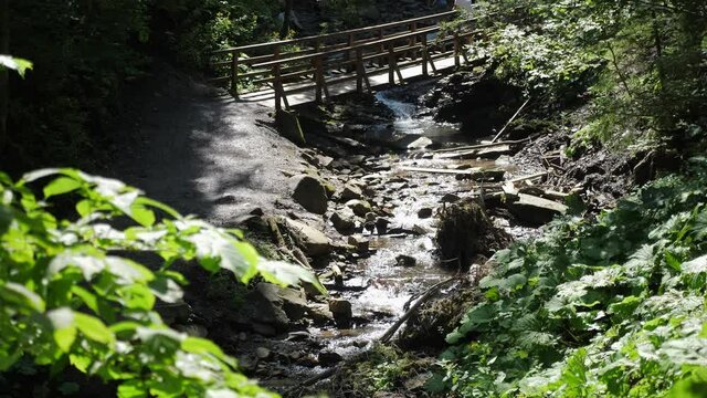 Fairytale mountain river flowing under bridge with people on it on a sunny day