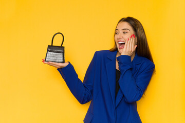 Young woman in elegant blue jacket is holding small purse and laughing.