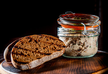 Jar of mackerel rillettes with toast on rustic wooden table dark background