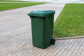 Plastic green garbage can for collecting garbage in the park. Mobile trash can with wheels