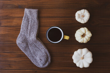 Autumn flat lay with a cup of hot drink, white mini pumpkins and warm wool socks on wooden rustic background.