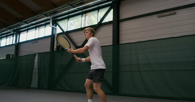 A man plays tennis, hitting ball by ball with a racket, playing indoor