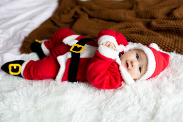 Closeup portrait of newborn baby. Cute Caucasian baby girl 4-5 months old in Santa costume lying on knitted cozy blanket on bed. Merry Christmas xmas and happy new year 2022