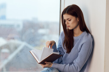 woman reading a book near the window with a cup of drink rest
