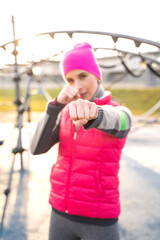 Obraz premium Young caucasian fit woman in pink fitness clothes boxing with hands in fists and makes punches on modern athletic field outdoors on sunrise on cold autumn, winter or spring morning. Sports, training