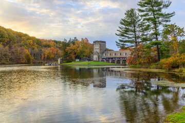 Fototapeta na wymiar Beautiful lakeside view of Fall foliage and an old building in a park in the morning.