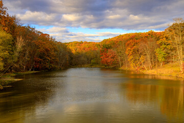 Fototapeta premium A lake and woodland area featuring beautiful Fall foliage with a dramatic sky during early evening.