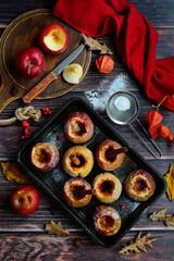 A vertical view of red apples with cinnamon baked on a baking sheet. Dark wood background